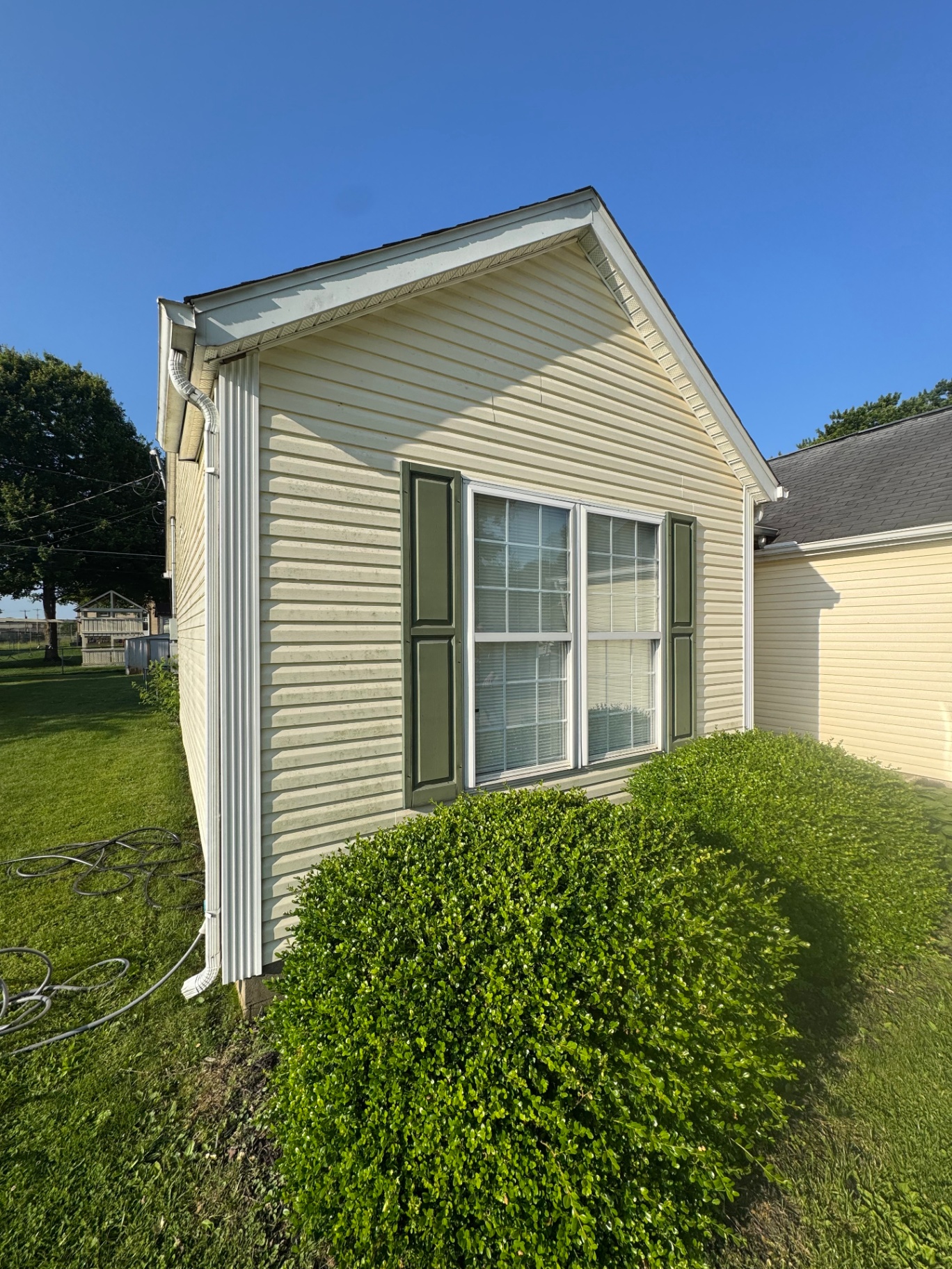 Yellow siding with dirt around a shuttered window